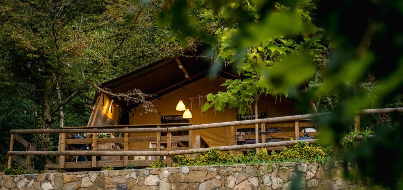 Safaritent Desert Lodge op Camping Delle Rose in Italië, omgeven door groen met een houten terras.