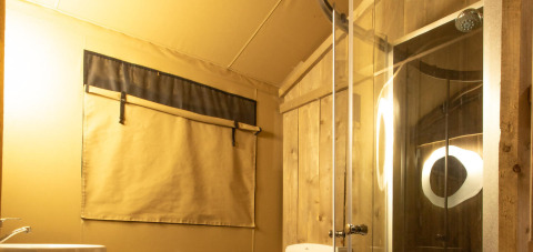 Baño en una tienda safari Wood Lodge en Camping Delle Rose, Italia, con paredes de madera y ducha moderna.
