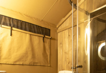 Baño en una tienda safari Wood Lodge en Camping Delle Rose, Italia, con paredes de madera y ducha moderna.