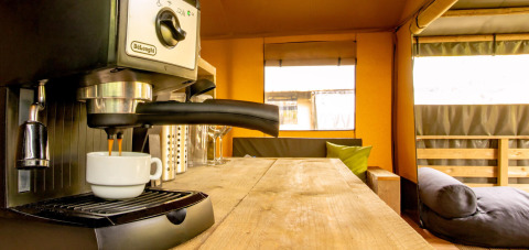 Cafetera preparando espresso en el interior de madera de la tienda safari Wood Lodge en Camping Delle Rose, Italia.