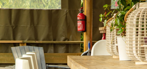 Interno di tenda safari, Wood Lodge, Camping Delle Rose, Italia, con tavolo, sedie e estintore a muro.