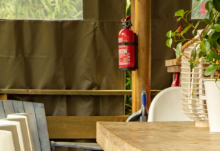 Interno di tenda safari, Wood Lodge, Camping Delle Rose, Italia, con tavolo, sedie e estintore a muro.