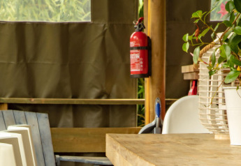 Interior de tienda safari, Wood Lodge, Camping Delle Rose, Italia, con mesa, sillas y extintor visible.