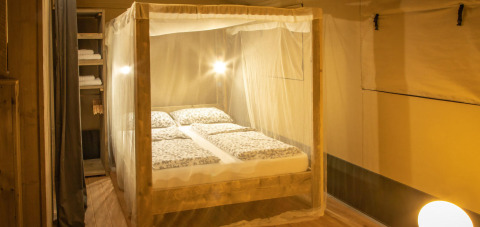 Camera da letto nella tenda safari Wood Lodge al Camping Delle Rose, Italia, con letto a baldacchino e zanzariera.