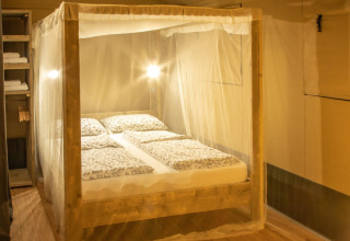 Camera da letto nella tenda safari Wood Lodge al Camping Delle Rose, Italia, con letto a baldacchino e zanzariera.