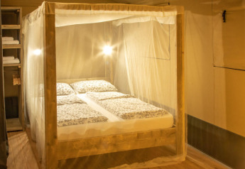 Dormitorio en la tienda safari Wood Lodge en Camping Delle Rose, Italia, con cama con dosel y mosquitera.