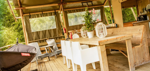 Zona de comedor exterior en la tienda safari Wood Lodge en Camping Delle Rose, Italia, con muebles de madera.