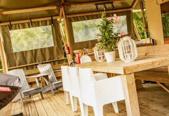 Zona de comedor exterior en la tienda safari Wood Lodge en Camping Delle Rose, Italia, con muebles de madera.