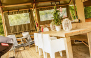 Zona de comedor exterior en la tienda safari Wood Lodge en Camping Delle Rose, Italia, con muebles de madera.