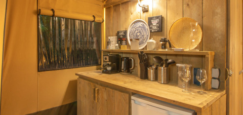 Acogedora cocina de tienda safari en Wood Lodge, Camping Delle Rose, Italia, con paneles y utensilios de madera.