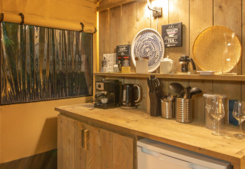Acogedora cocina de tienda safari en Wood Lodge, Camping Delle Rose, Italia, con paneles y utensilios de madera.