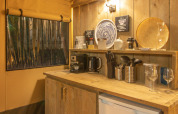 Acogedora cocina de tienda safari en Wood Lodge, Camping Delle Rose, Italia, con paneles y utensilios de madera.