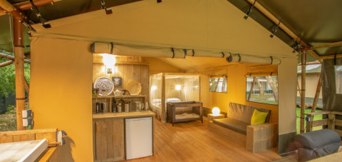Interior de la tienda safari Wood Lodge en Camping Delle Rose, Italia, con cocina, sofá y cama.