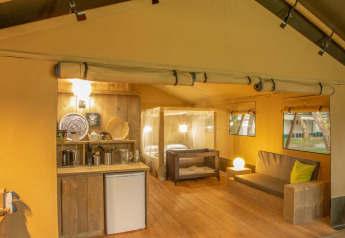 Interior de la tienda safari Wood Lodge en Camping Delle Rose, Italia, con cocina, sofá y cama.