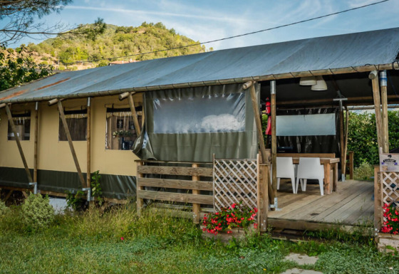 Tienda safari llamada Wood Lodge con terraza cubierta de madera, rodeada de colinas verdes y flores rojas.
