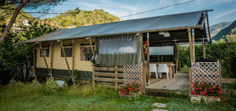 Safari tent called Wood Lodge featuring a covered wooden deck, surrounded by green hills and colorful flowers.