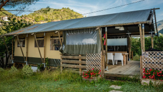 Tienda safari llamada Wood Lodge con terraza cubierta de madera, rodeada de colinas verdes y flores rojas.