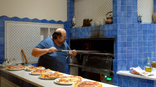 Man baking pizzas in a blue-tiled kitchen at Camping Delle Rose holiday park in Liguria, Italy.