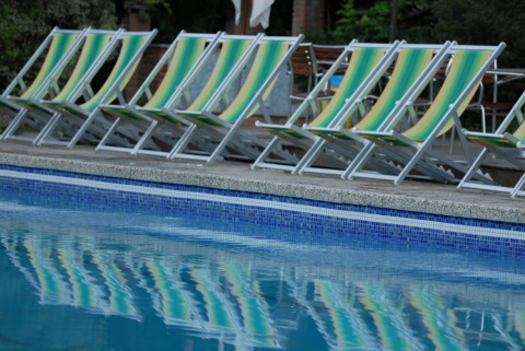 Fila de tumbonas vacías con rayas verdes y amarillas junto a la piscina en Camping Delle Rose, Liguria, Italia.