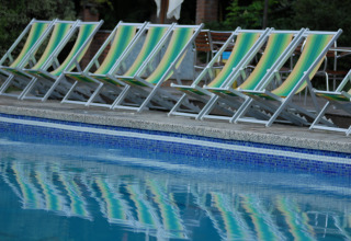 Row of empty green-yellow striped deck chairs by the pool at Camping Delle Rose, Liguria, Italy.