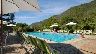 Buitenbad met ligstoelen en parasols, omgeven door heuvels bij Camping Delle Rose in Ligurië, Italië.