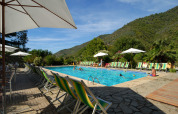 Buitenzwembad met ligstoelen en parasols, omringd door heuvels bij Camping Delle Rose in Ligurië, Italië.