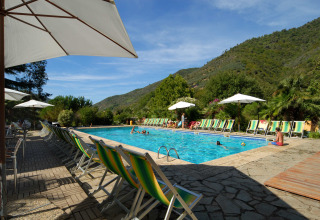 Buitenbad met ligstoelen en parasols, omgeven door heuvels bij Camping Delle Rose in Ligurië, Italië.