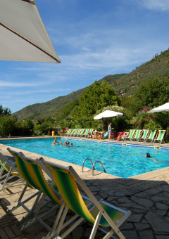 Outdoor swimming pool with sun loungers and umbrellas, surrounded by hills at Camping Delle Rose in Liguria, Italy.