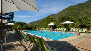 Outdoor swimming pool with sun loungers and umbrellas, surrounded by hills at Camping Delle Rose in Liguria, Italy.