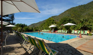 Piscina al aire libre con tumbonas y sombrillas, montañas de fondo, en Camping Delle Rose, Liguria, Italia.