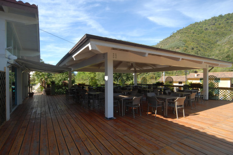Terrazza coperta con tavoli e sedie al Camping Delle Rose in Liguria, Italia, circondata da colline verdi.