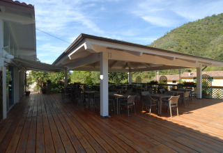 Terrasse extérieure couverte avec tables et chaises au Camping Delle Rose, en Ligurie, Italie, entourée de collines.
