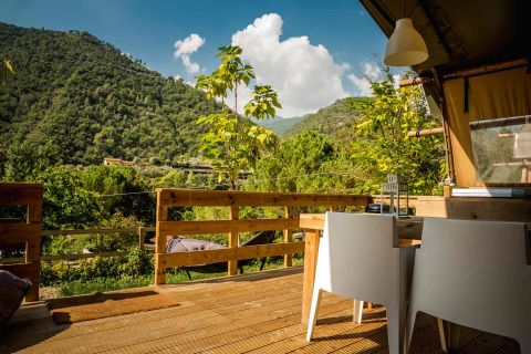 Houten terras met tafel en stoelen op Camping Delle Rose, Ligurië, Italië, met zicht op groene heuvels.