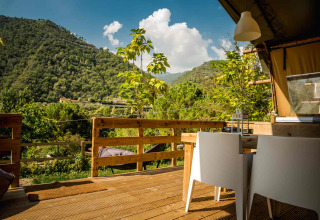 Wooden terrace with table and chairs at Camping Delle Rose, Liguria, Italy, overlooking green hills.
