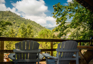 Two chairs on a wooden terrace overlooking lush green hills near Isolabona, Liguria, Italy.