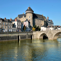 Foto einer Altstadt mit einem Schloss, alten Gebäuden und einer Steinbrücke über einen Fluss bei Sonnenschein.