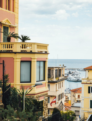 Vibrant buildings and a sea view with a marina near Isolabona, Liguria, Italy, under a partly cloudy sky.