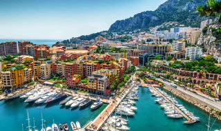 Marina with yachts and colorful buildings set against mountains near Isolabona, Liguria, Italy.