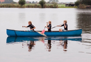Tre bambini remano in una canoa blu su un lago al Camping Vrijhaven Heeg, un villaggio vacanze in Frisia, Paesi Bassi.