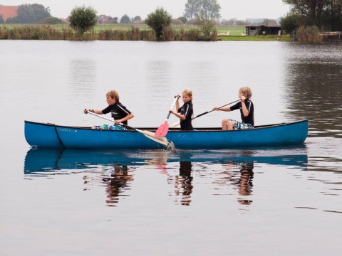 Tre bambini remano in una canoa blu su un lago al Camping Vrijhaven Heeg, un villaggio vacanze in Frisia, Paesi Bassi.