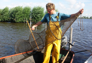 Een visser in gele broek met een net op een boot bij Camping Vrijhaven Heeg in Friesland, Nederland.