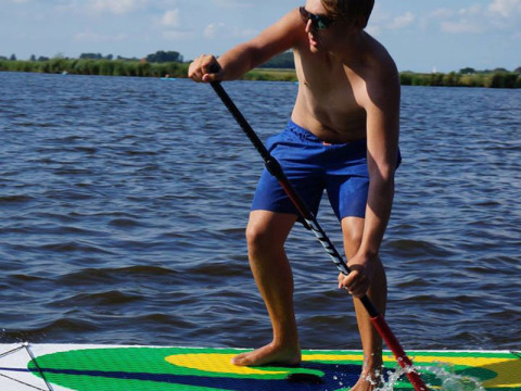 Uomo con pantaloncini blu fa paddleboarding su lago a Camping Vrijhaven Heeg, Friesland, Paesi Bassi.
