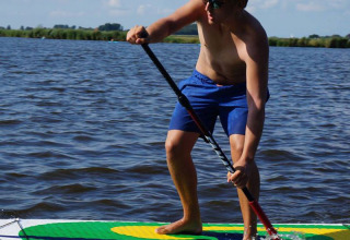 Uomo con pantaloncini blu fa paddleboarding su lago a Camping Vrijhaven Heeg, Friesland, Paesi Bassi.