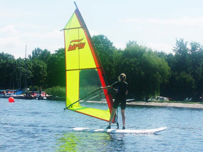 Person windsurfing on lake at Camping Vrijhaven Heeg, a holiday park in Friesland, Netherlands, with green sail.