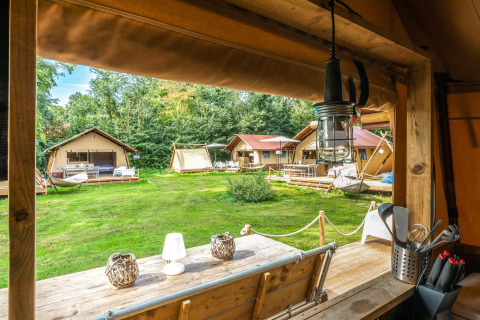 Vista desde dentro de una tienda Safari, Cozy Lodge + sanitario, con otras tiendas y césped verde afuera.