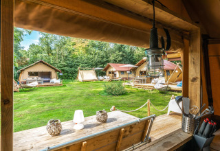 Blick aus einem Safari-Zelt, Cozy Lodge + Sanitär, auf andere Zelte und grüne Umgebung im Freien.