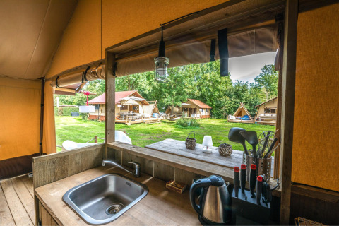 Vista dalla cucina della tenda safari Cozy Lodge con servizi igienici e altre tende su prato verde.