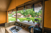 Vista desde la cocina del safari tent Cozy Lodge con baño, mostrando otras tiendas en el césped.