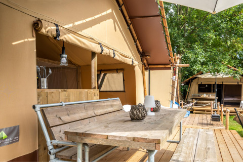 Terraza al aire libre de la tienda safari Cozy Lodge con mesa de madera, bancos y zona sanitaria privada.
