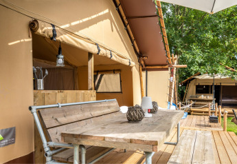 Terraza al aire libre de la tienda safari Cozy Lodge con mesa de madera, bancos y zona sanitaria privada.